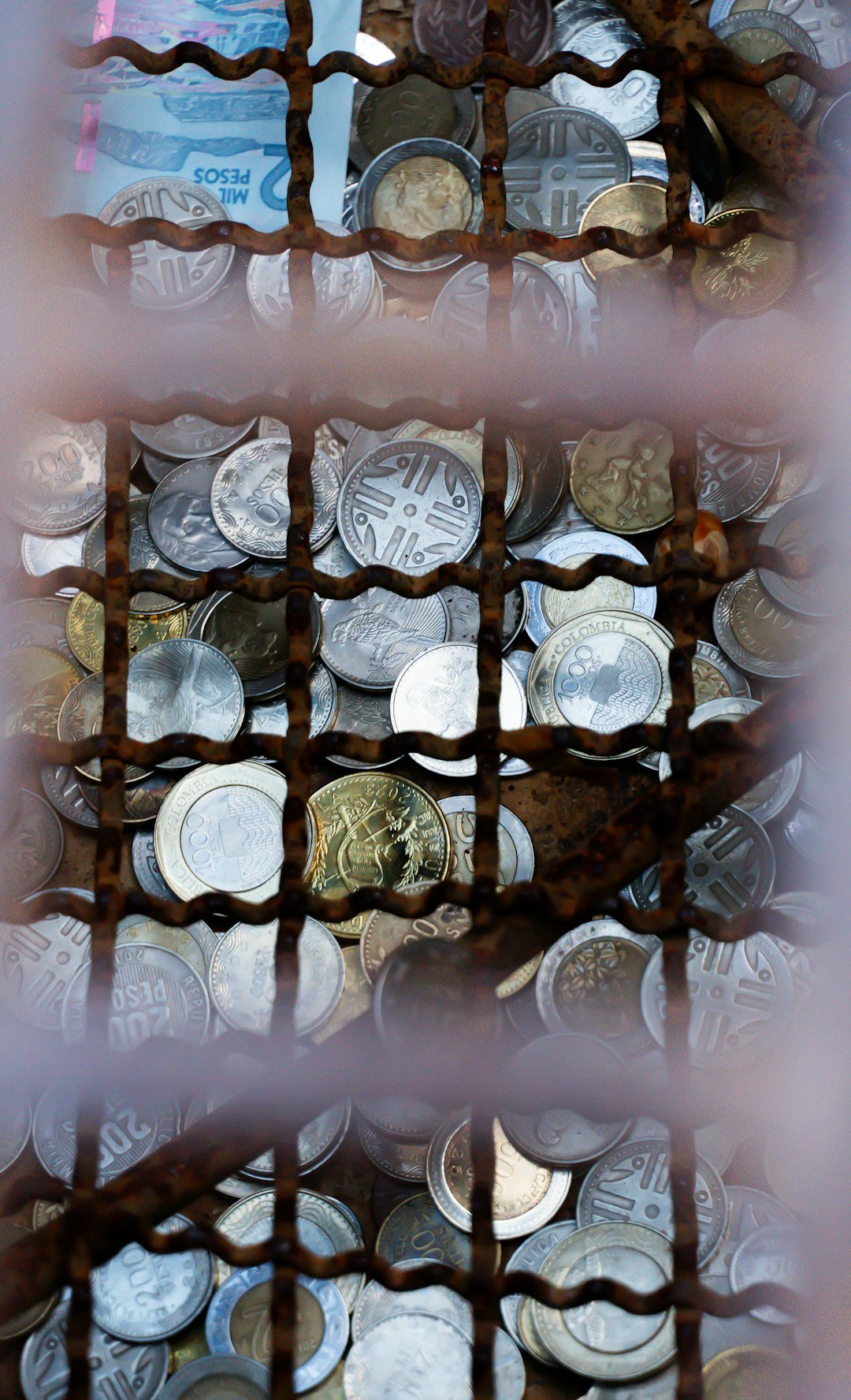 Pile of coins and bills behind a rusty metal grate.