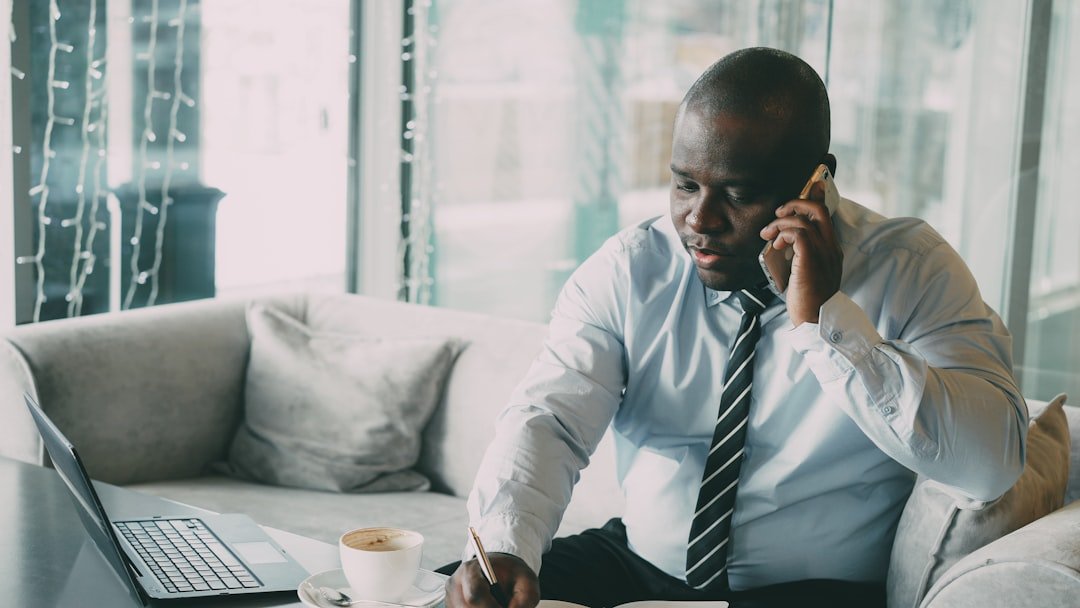 Man in shirt and tie talking on phone at desk.