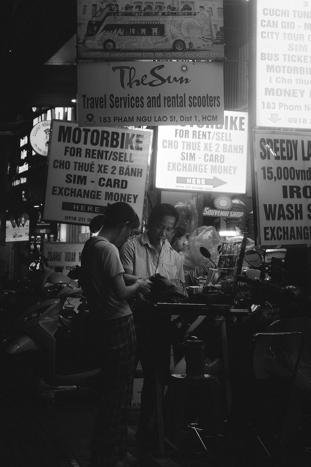 Two people stand near motorbikes under bright signs