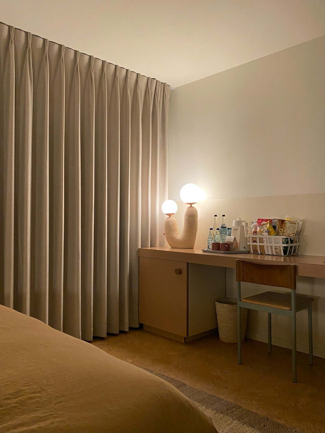 Hotel room desk with snacks, drinks, and lamp.