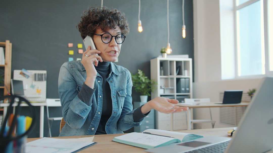Woman talking on phone at desk with laptop.