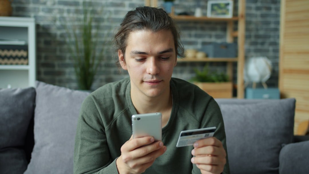 Young man using smartphone and credit card for online shopping.