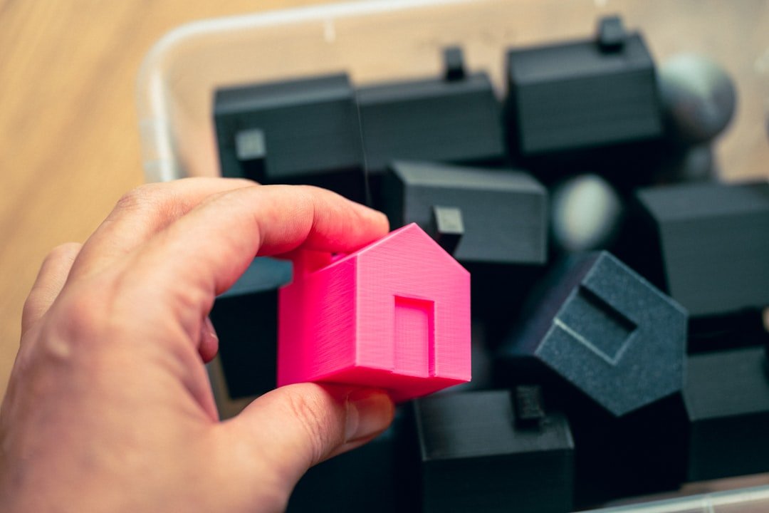 A person holding a pink house in front of a pile of black cubes