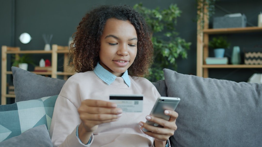 Young woman holding credit card and smartphone indoors