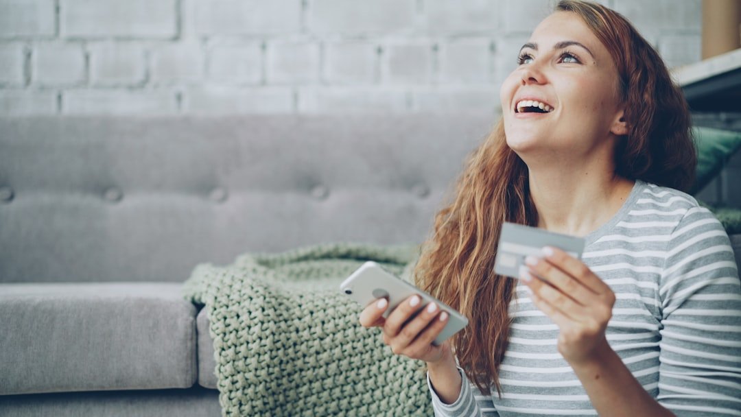 A happy woman holding a credit card and smartphone.